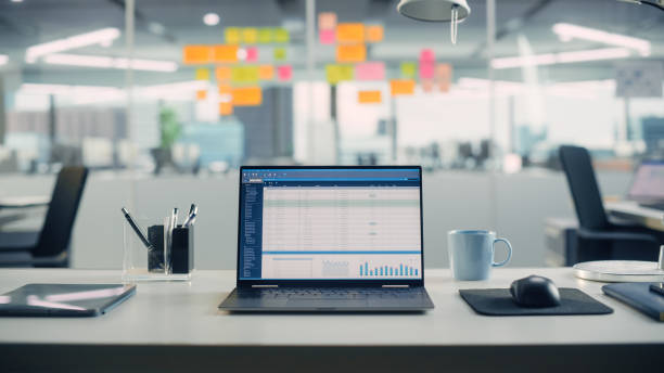 Laptop Computer with Financial Analytical Spreadsheet Application Standing on the Desk in the Modern Creative Office. In the Background Glass Wall with Colorful Planning Notes.